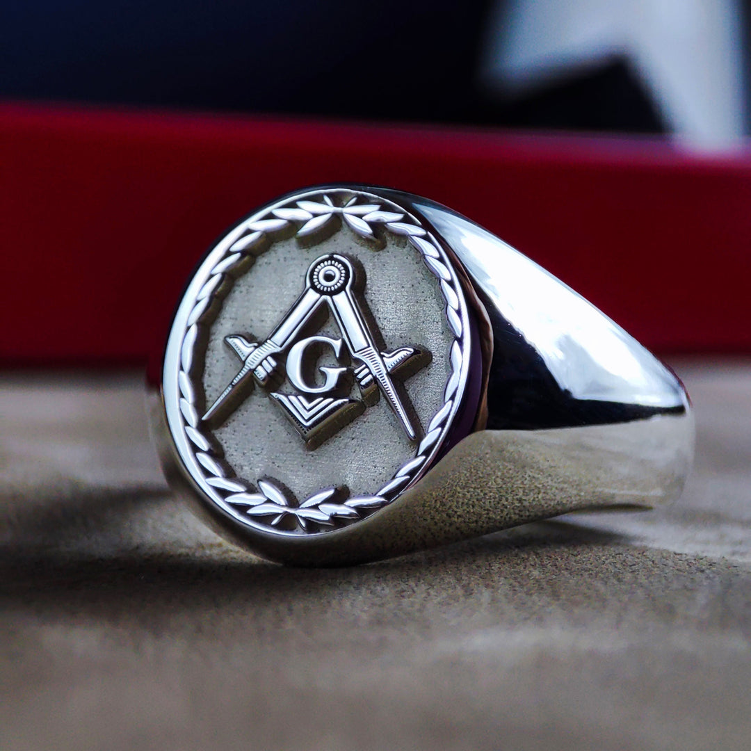 This silver Masonic ring features a detailed engraved leaf pattern, symbolizing growth and wisdom. Designed for Freemasons, this signet ring carries the iconic square and compass emblem, representing fraternity and enlightenment. Crafted in sterling silver, this elegant lodge ring is a perfect addition to any Masonic collection, making it a meaningful and symbolic piece for members and collectors alike.