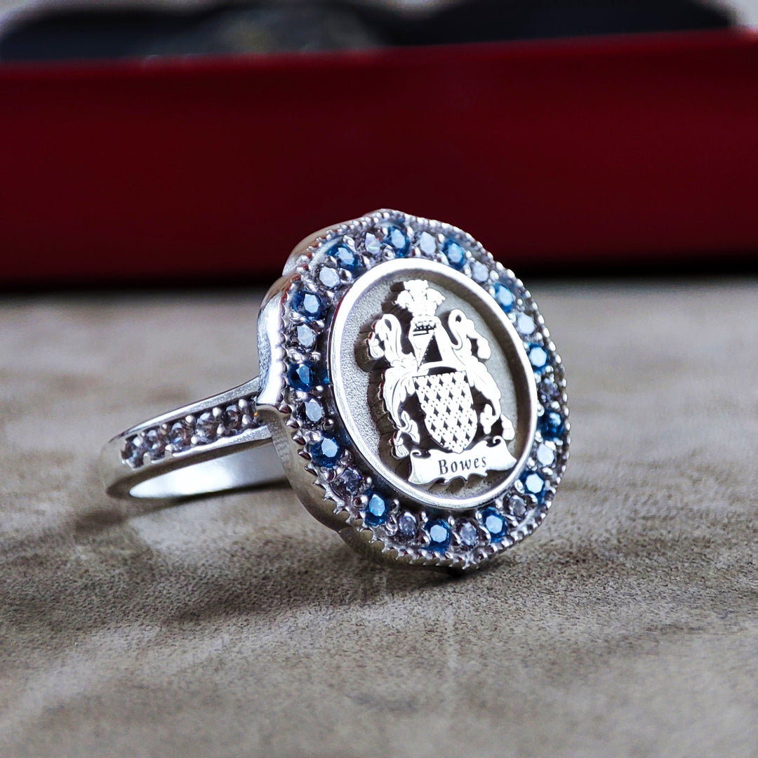 Custom family crest ring for women, with a central stone and engraved coat of arms in silver. This elegant ring honors lineage and makes a timeless addition to any jewelry collection.