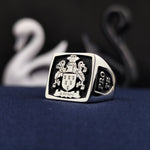 Load image into Gallery viewer, This antique-style silver signet ring features a square face with a black enamel finish, highlighting an intricately engraved family crest. A timeless and meaningful jewelry piece, this coat of arms ring is designed for those who embrace legacy and tradition. A bold and sophisticated heirloom, perfect for men who appreciate historical elegance and craftsmanship.

